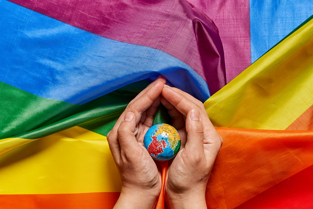 Hand holding globe on the rainbow flag - symbol of pride month in the world