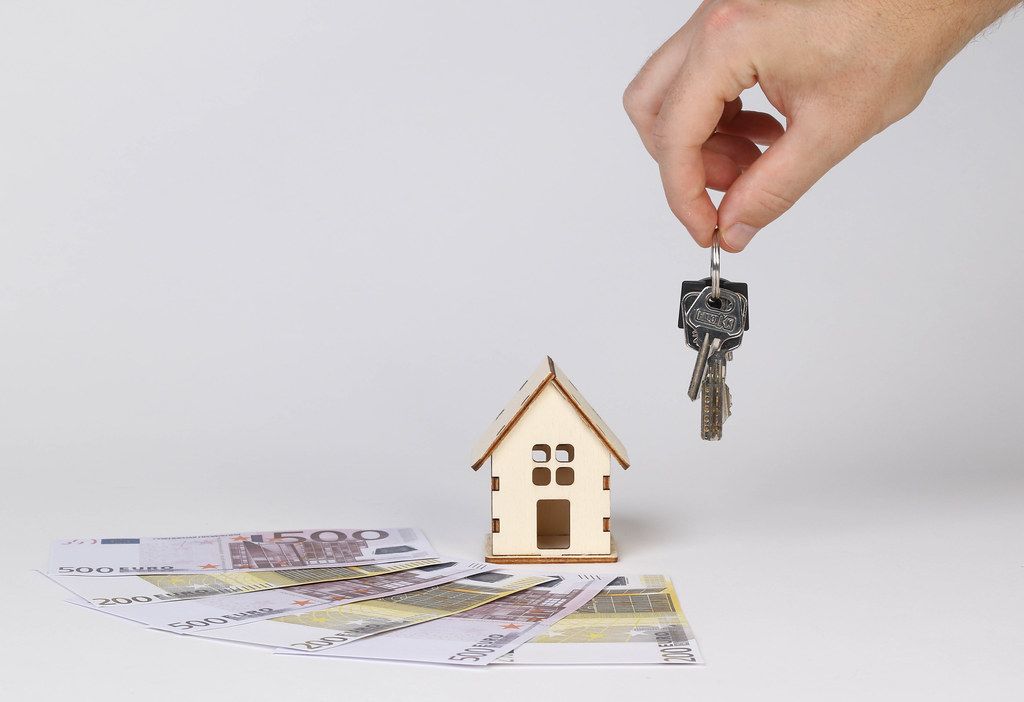 Hand holding keys and tiny wooden house with Euro banknotes