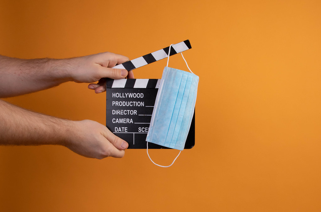 Hand holding movie clapper and medical face mask on orange background