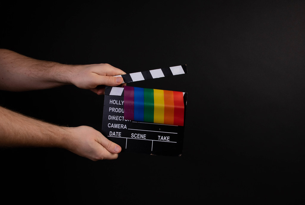 Hand holding movie clapper and rainbow flag on black background