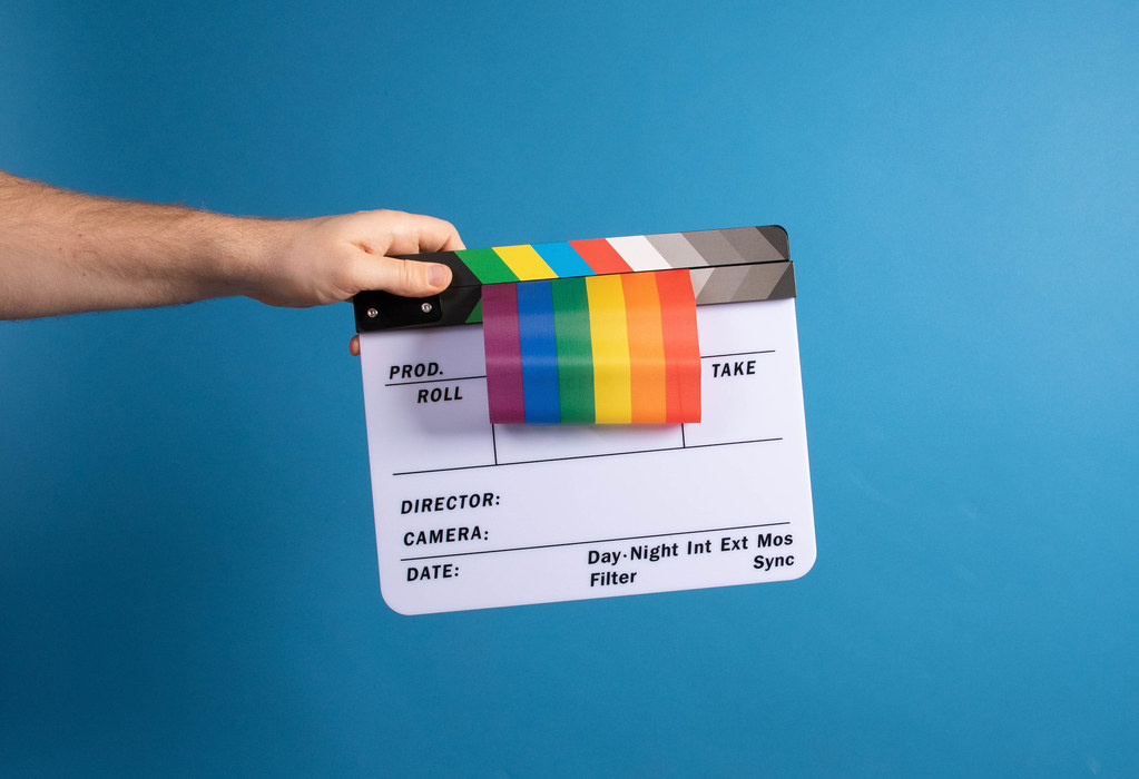 Hand holding movie clapper and rainbow flag on blue background