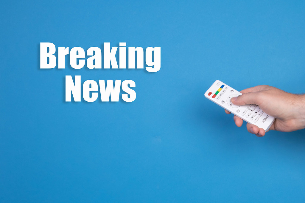 Hand holding remote control and Breaking news text on blue background