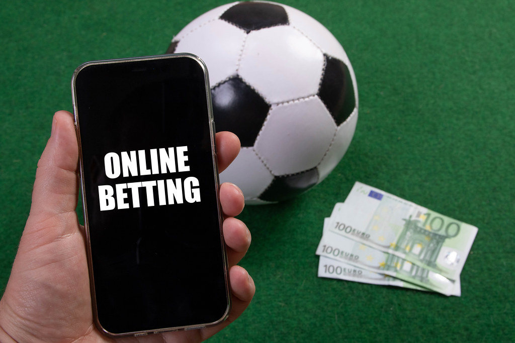 Hand holding smartphone with Online Betting text over a soccer ball and Euro banknotes