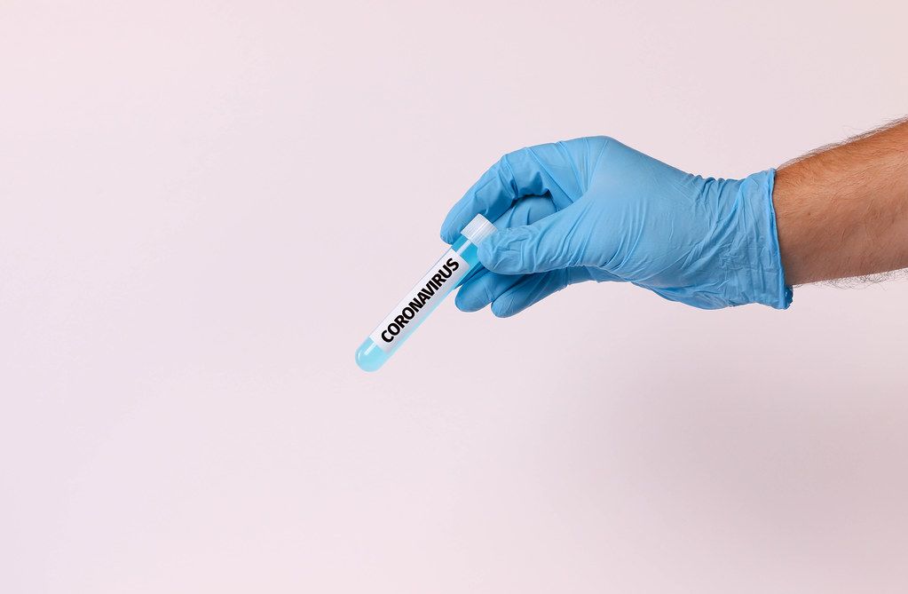 Hand holding test tube with text CORONAVIRUS on white background