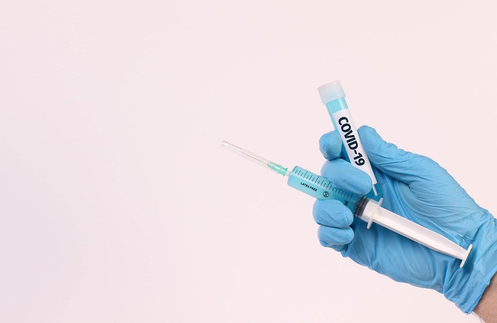 Hand holding test tube with text COVID-19 and syringe on white background