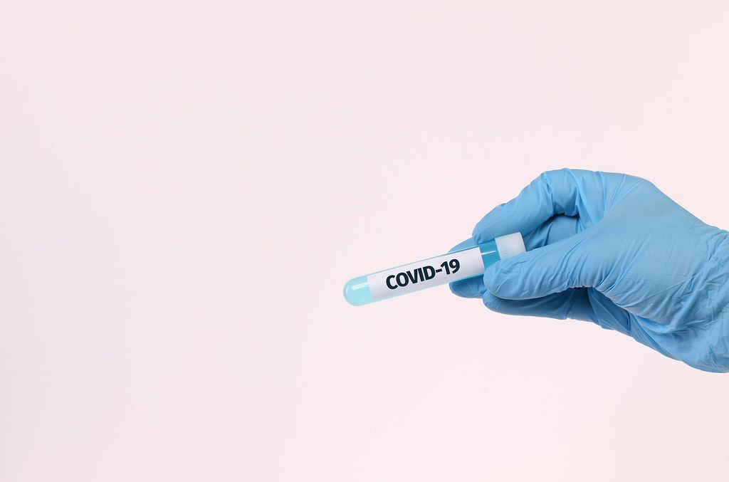 Hand holding test tube with text COVID-19 on white background