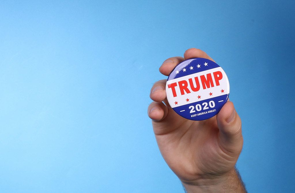 Hand holding Trump 2020 badge on blue background