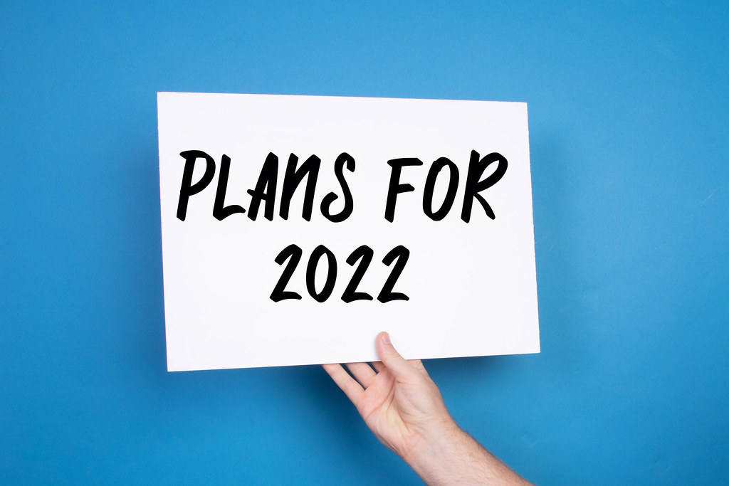 Hand holding white banner with Plans for 2022 text on blue background