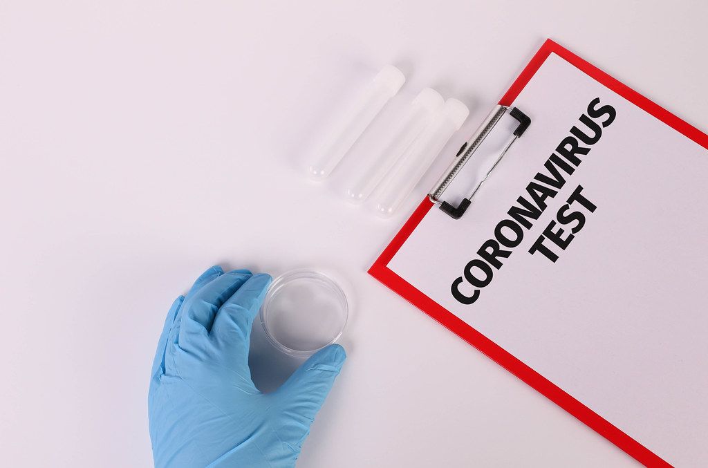 Hand in blue medical glove holding empty test tube and clipboard with Coronavirus test text