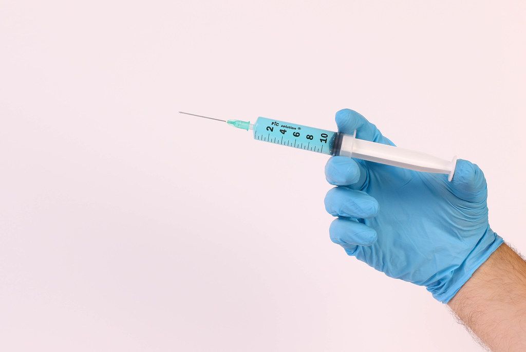Hand in medical glove holding syringe with blue fluid
