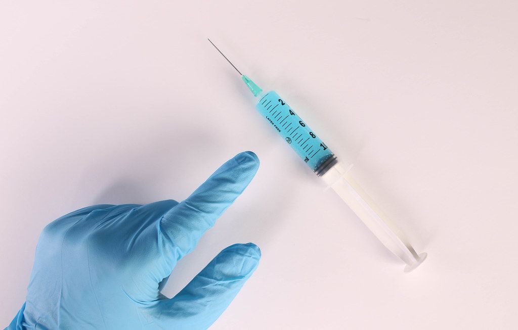 Hand in medical gloves pointing at syringe with blue fluid