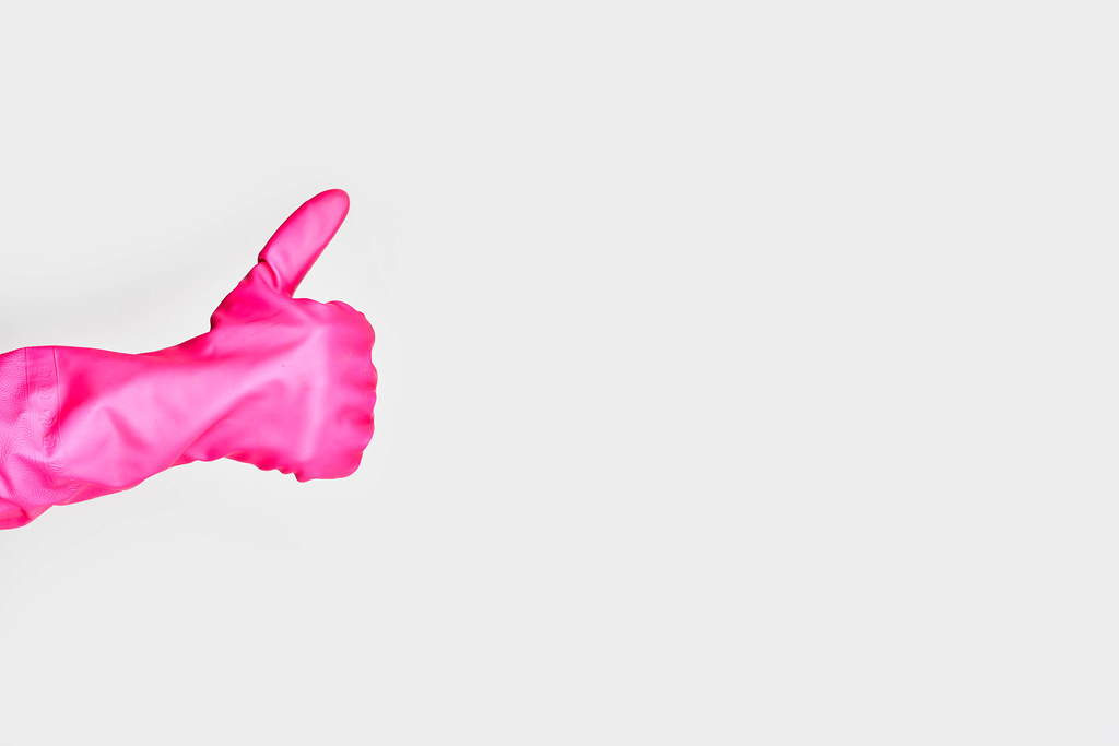 Hand in pink rubber glove showing thumbs-up hand gesture against the white background