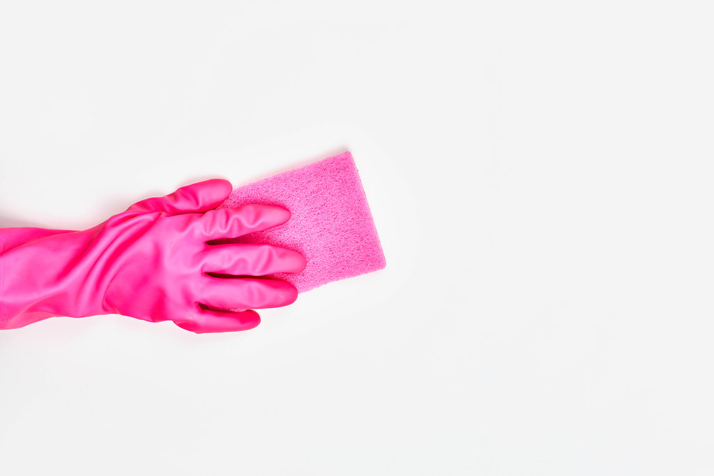 Hand in pink rubber gloves washing surface with a pink sponge