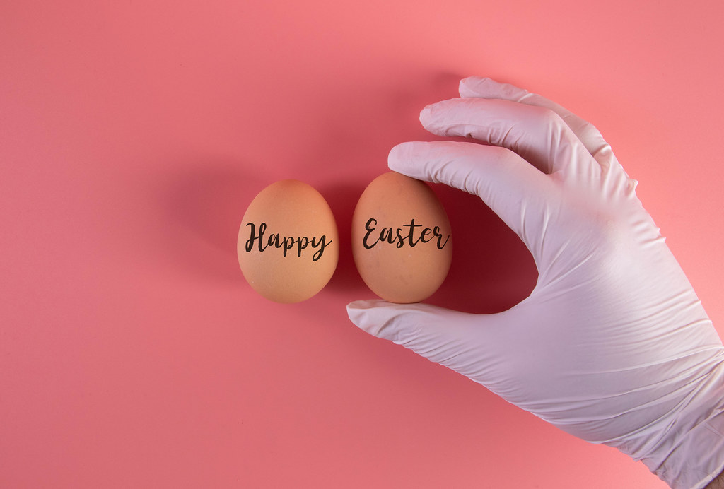 Hand in protective gloves with two eggs and Happy Easter text