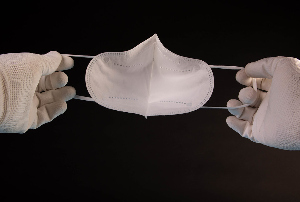 Hand in white gloves holding FFP2 medical face mask on black background