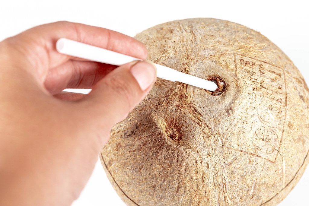 Hand inserts a straw into the coconut