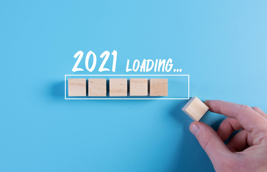 Hand putting wooden cube in progress bar with 2021 loading text