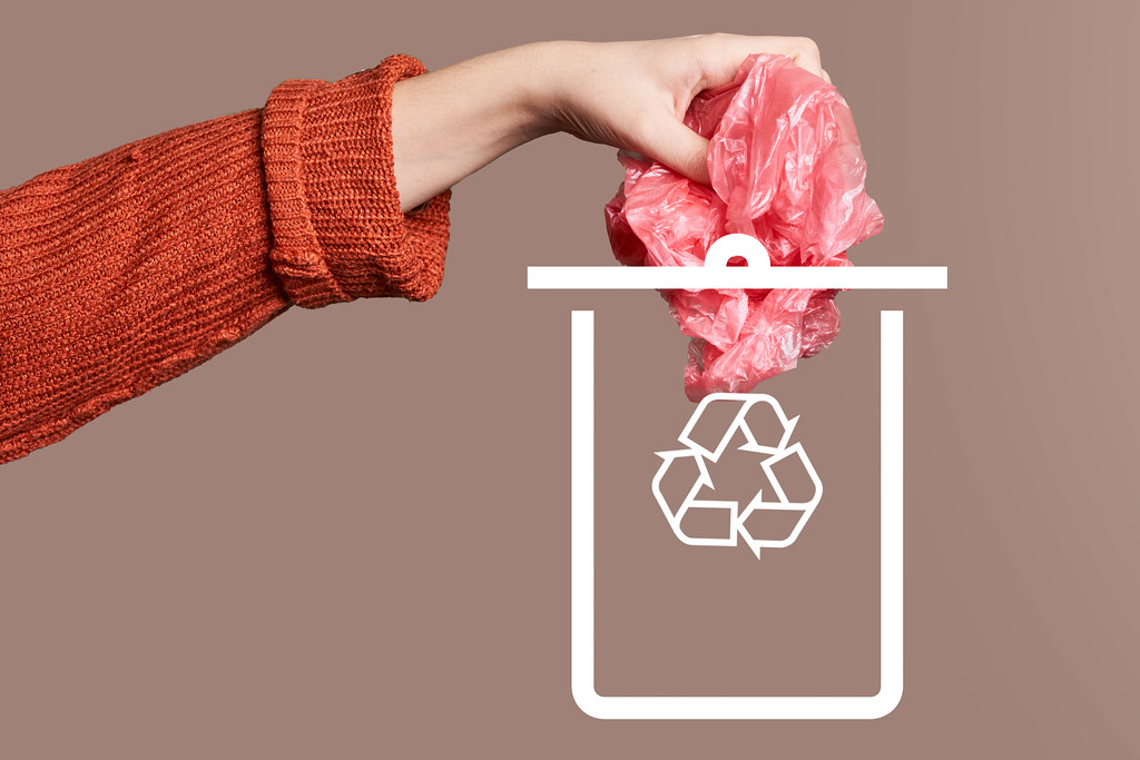 Hand throwing a plastic bag into drawn can. Concept of plastic recycling