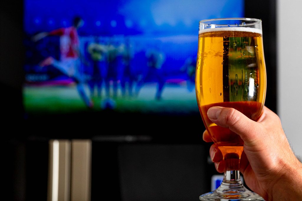 Hand with a glass of light beer on a blurred background of a football match