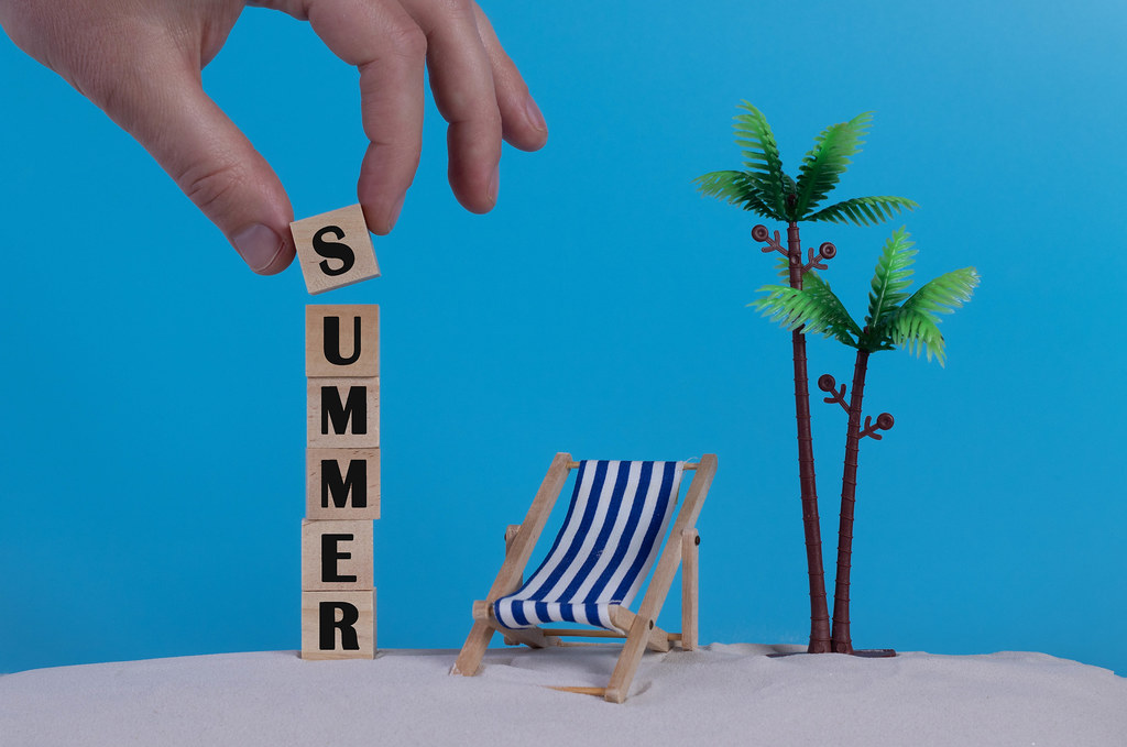 Hand with wooden blocks wiht Summer text and beach chair on blue background