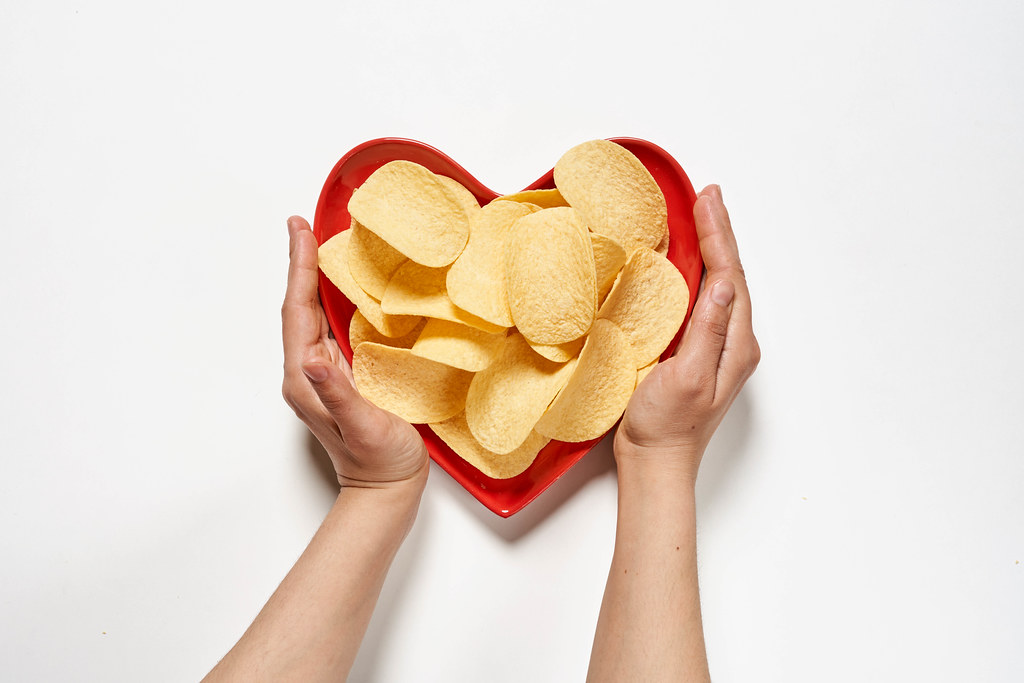 Hands hold heart-shaped plate full of crispy salty chips
