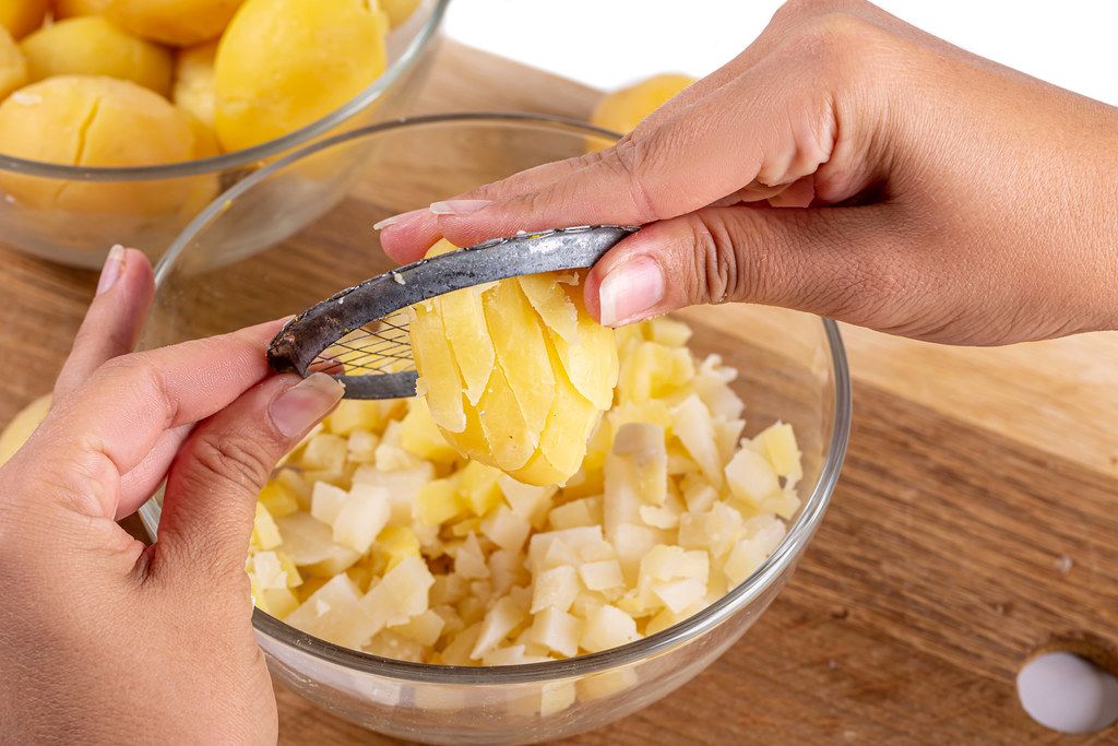Hands push boiled potatoes through the grate of a vegetable cutter