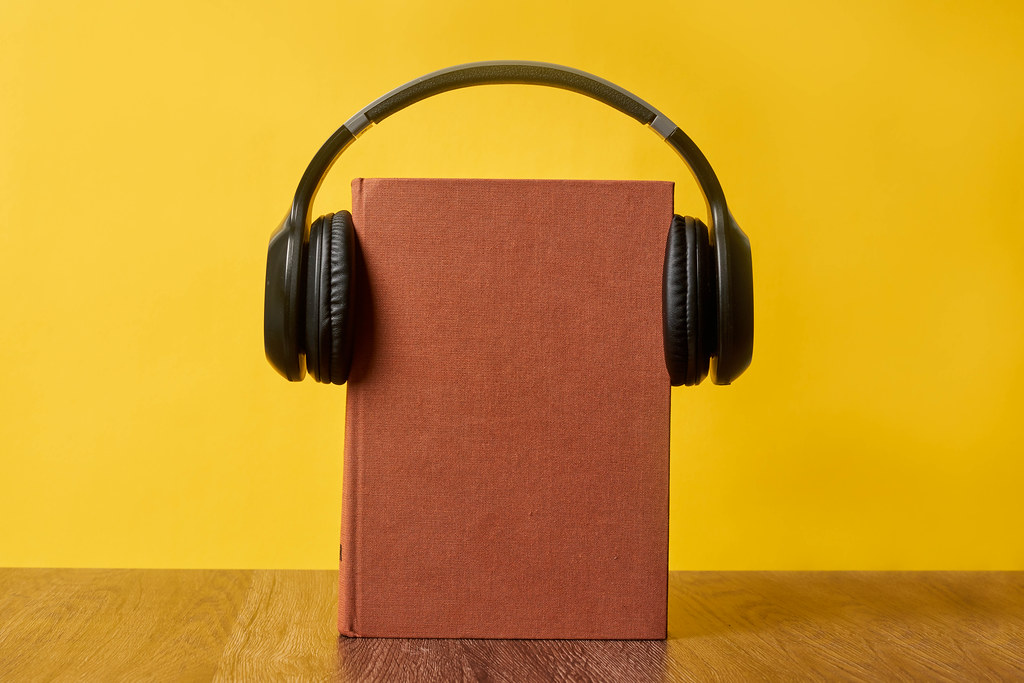 Headphones put over hardback book with empty cover on yellow background