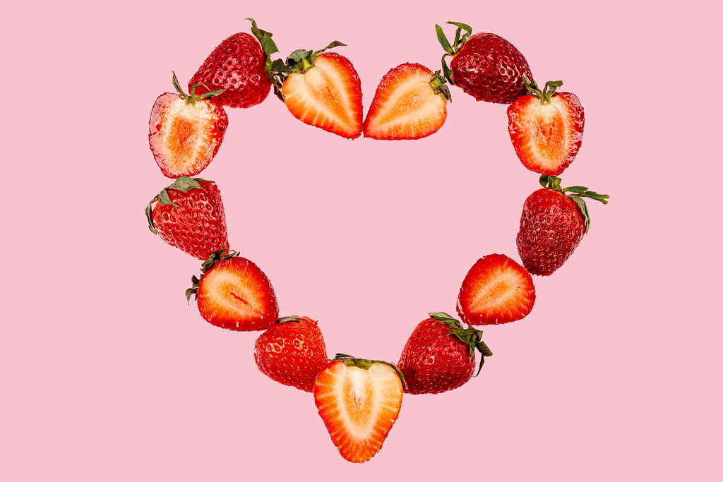 Heart made of halves of strawberries on a pink background, top view