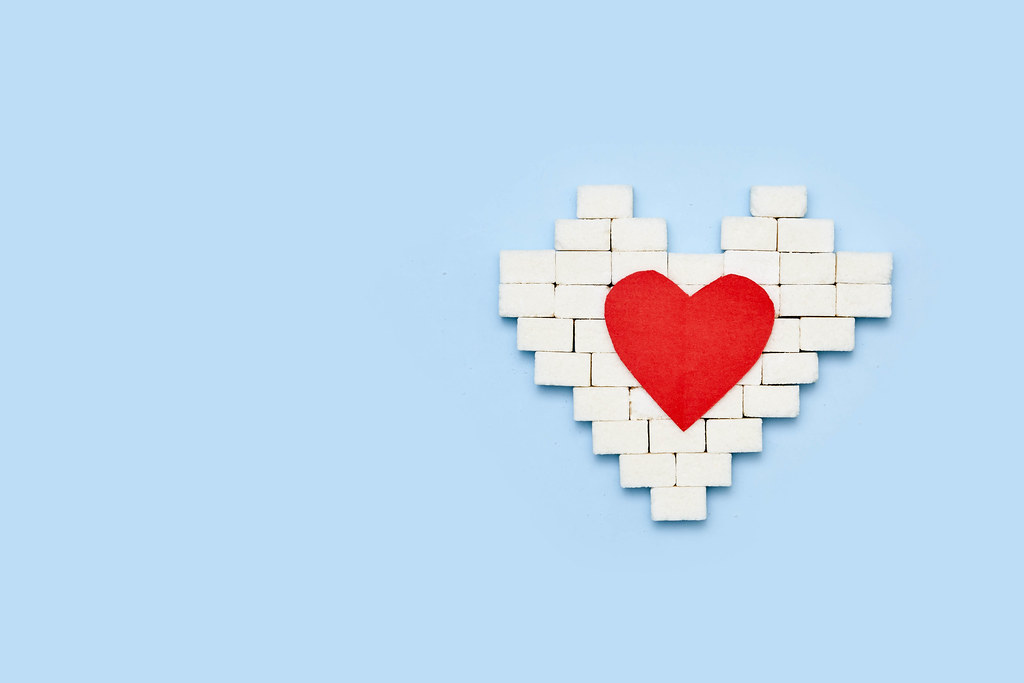 Heart shape made of sugar cubes and red heart paper cut on blue background