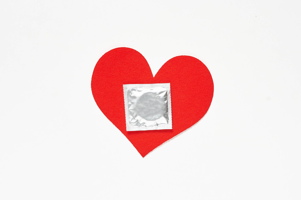 Heart shape paper cut and condom on white background