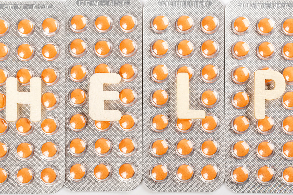Help from wooden letters on a background of orange pills in blisters