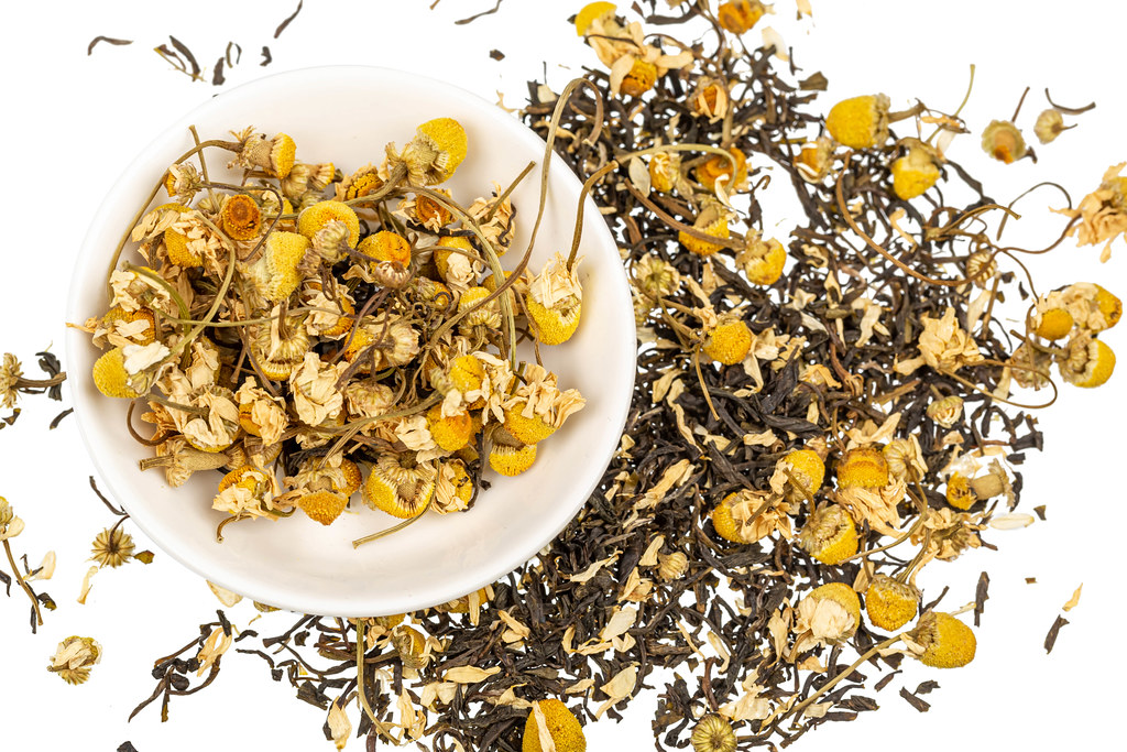 Herbal tea with dried chamomile flowers and black tea, top view