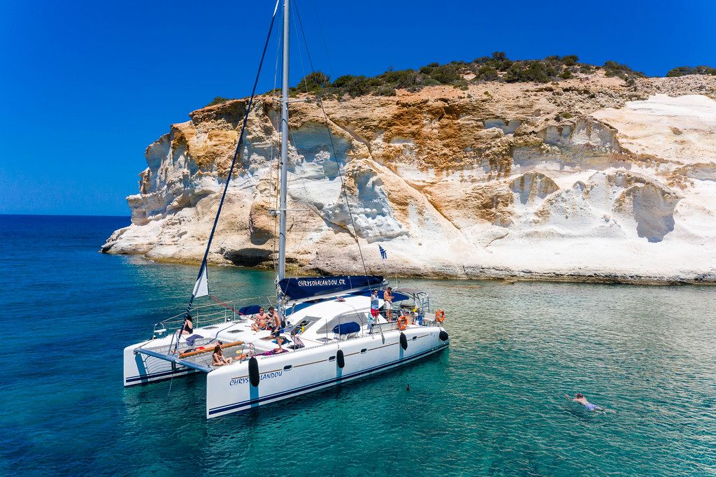 Holiday in Greece: tourists enjoying the sun and the turquoise waters of Milos from a sailing catamaran