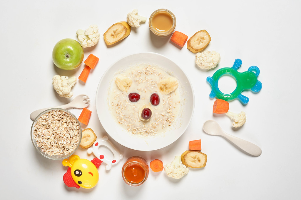 Homemade organic baby porridge and a pile of toys, vegetables and fruit cuts around