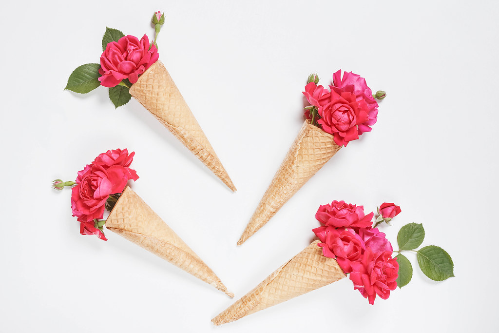 Ice cream cone with pink flowers and leaves on white background