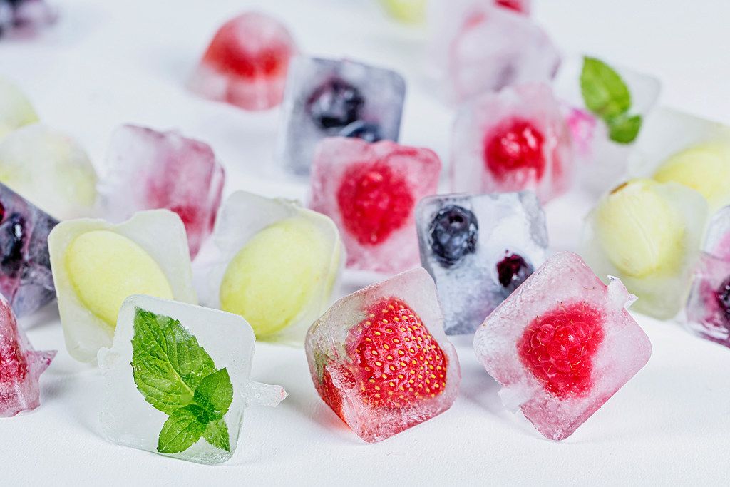 Ice cubes with different fruits, mint and berries frozen inside