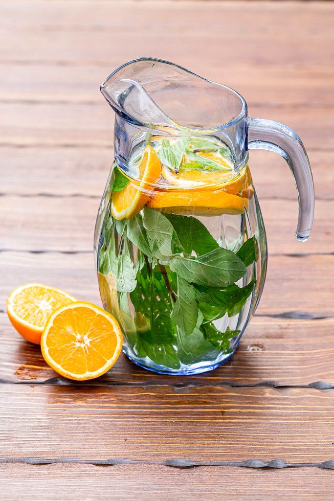 Jug with orange and mint lemonade on a wooden background
