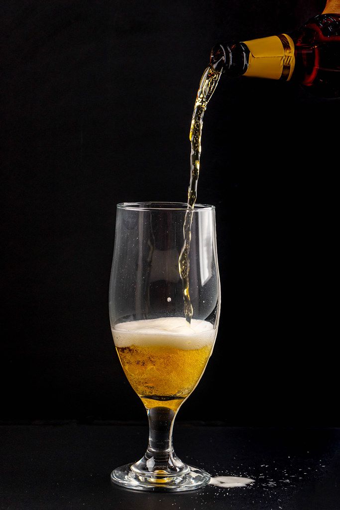 Light beer is poured into a glass on a black background