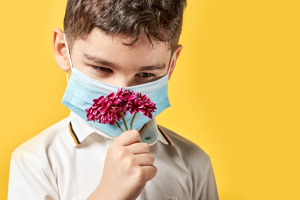Little kid with allergy wearing face mask and smelling flowers