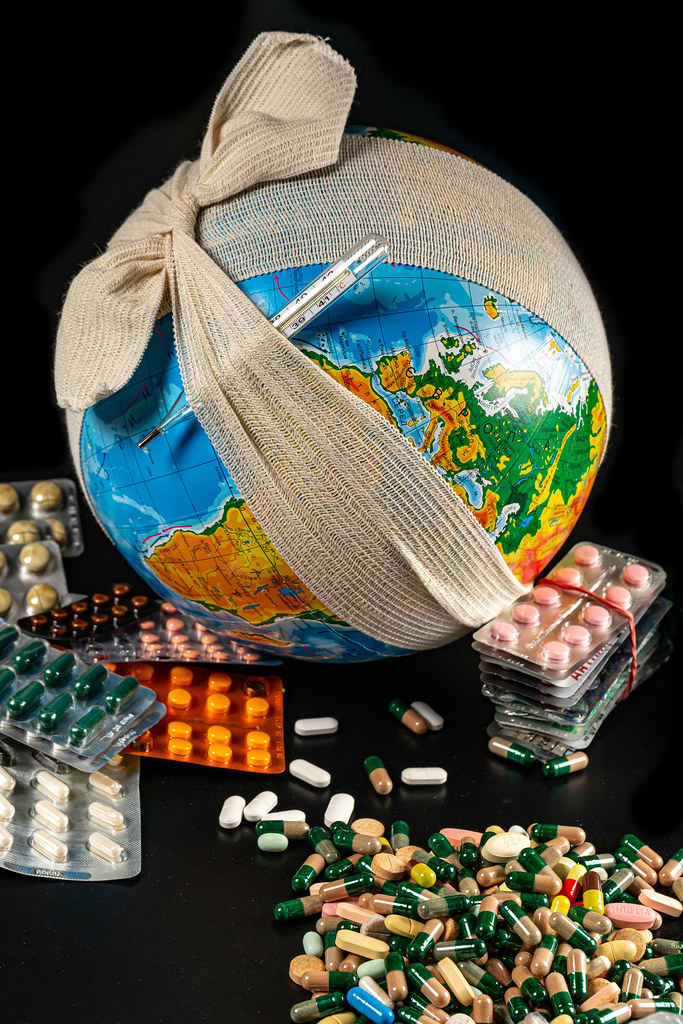 Lots of medical drugs pills and capsules on a dark background with a globe in an elastic bandage