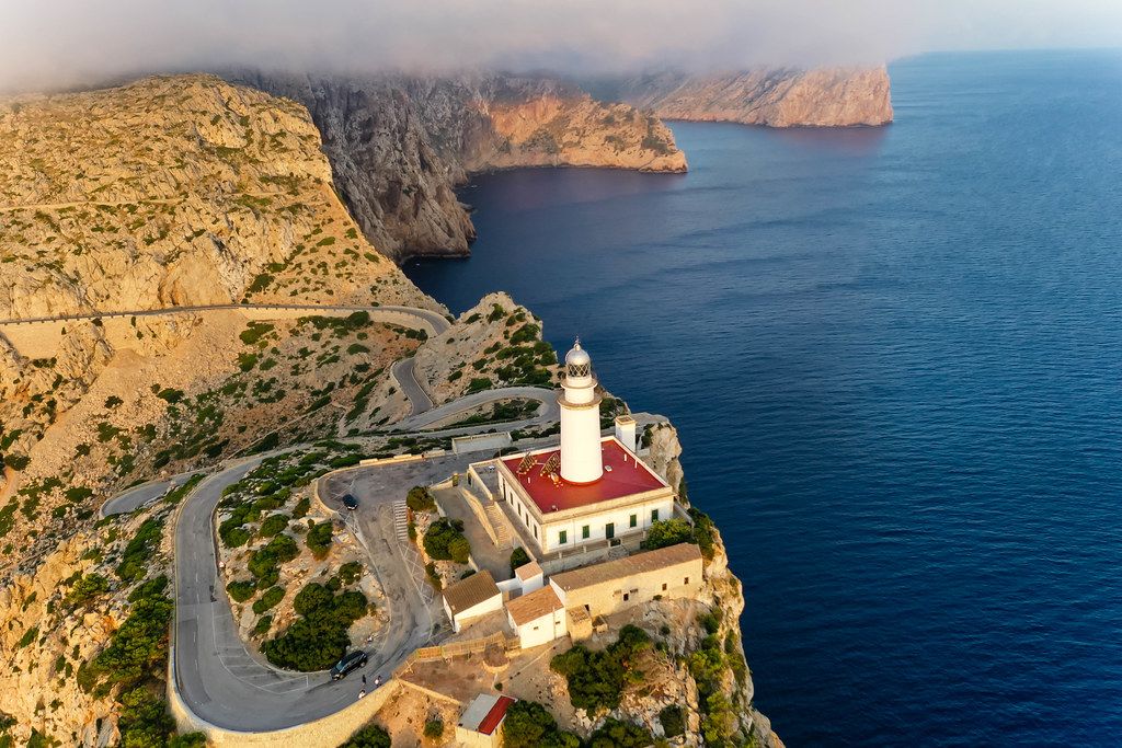Low clouds over the rocky cliffs at Cap de Formentor, lighthouse and winding road. Aerial view in Majorca
