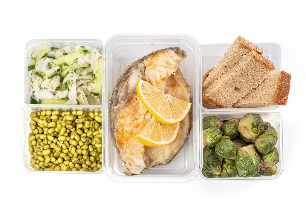 Lunch boxes with fish, vegetables, mung and black bread, top view