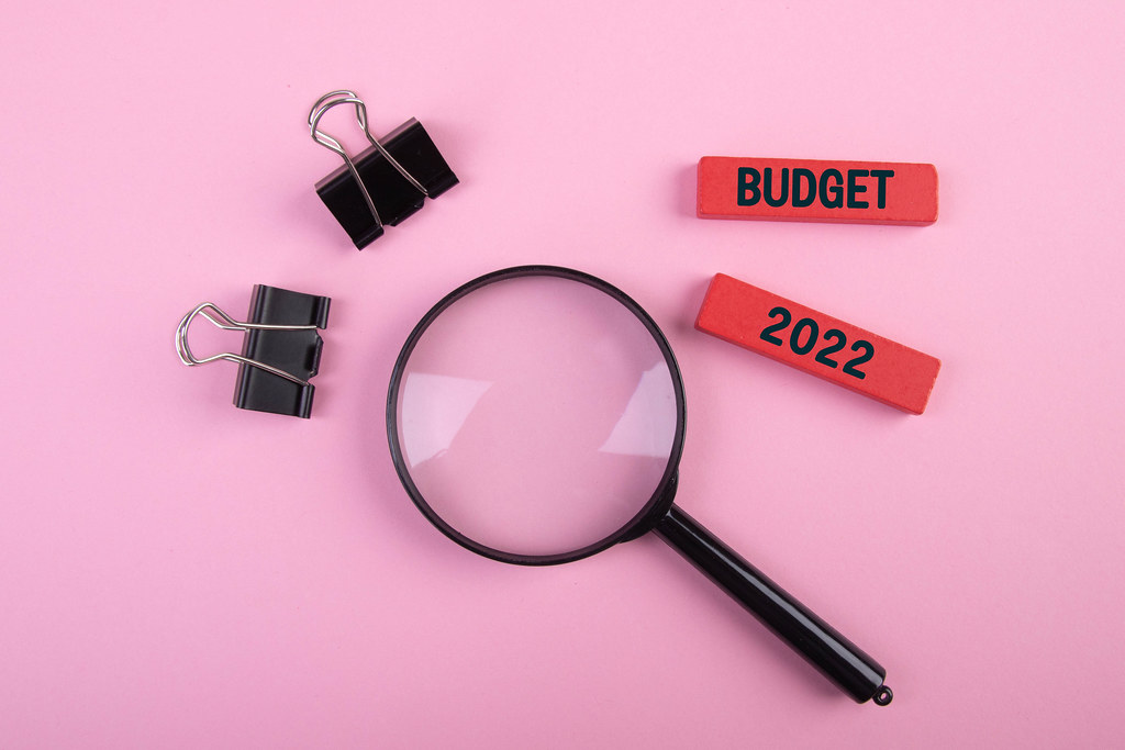Magnifying glass with paper clips and Budget 2022 text on pink background