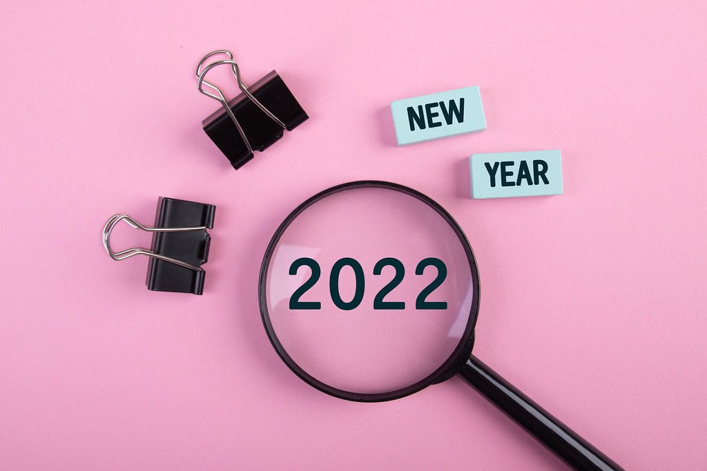 Magnifying glass with paper clips and New Year 2022 text on pink background