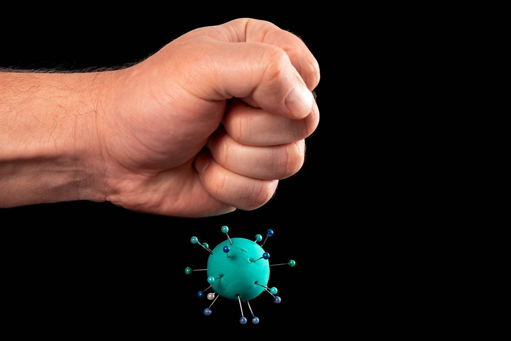 Male fist and model of plasticine virus on black background, concept of fighting coronavirus