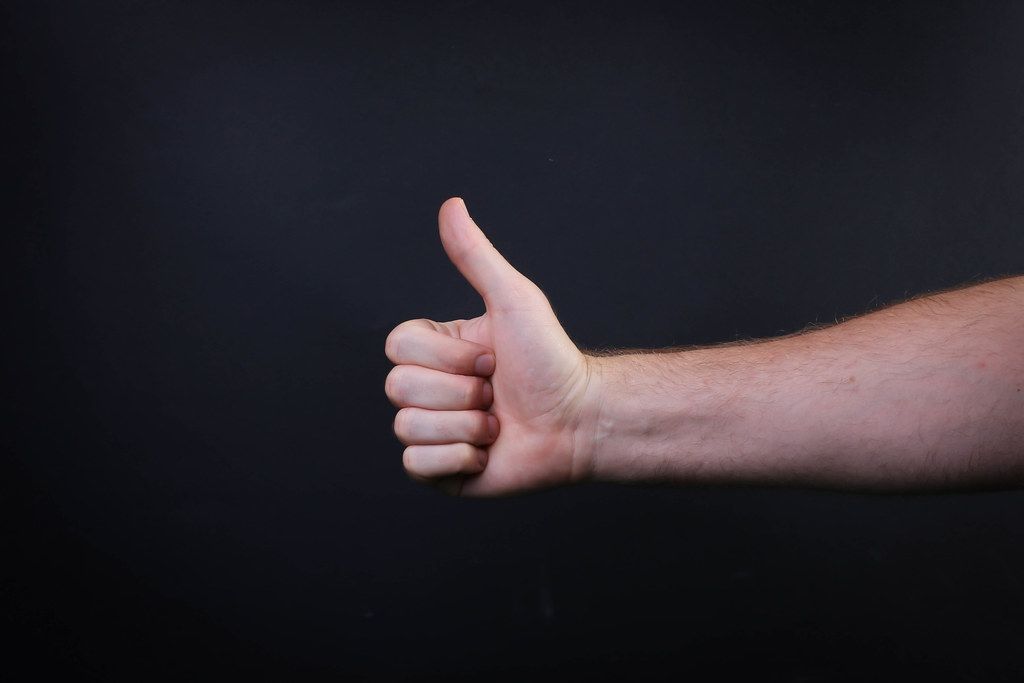 Male hand is showing a thumbs up gesture sign on black background