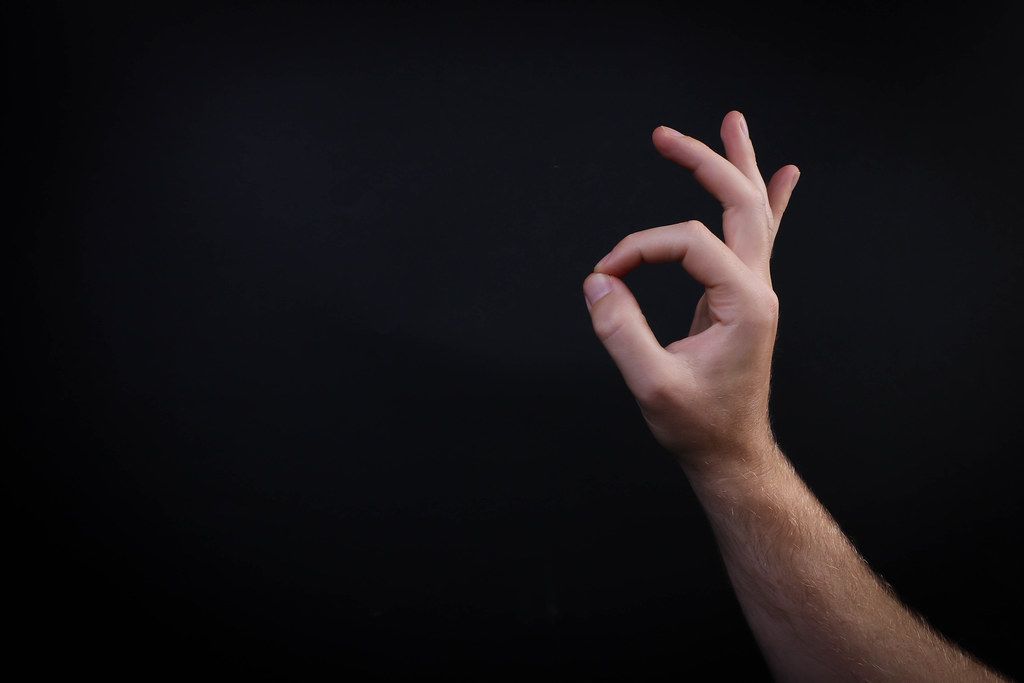 Male hand shows gesture OK on black background