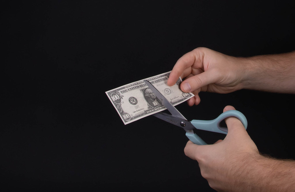 Man cutting 100 Dollar banknote with scissors