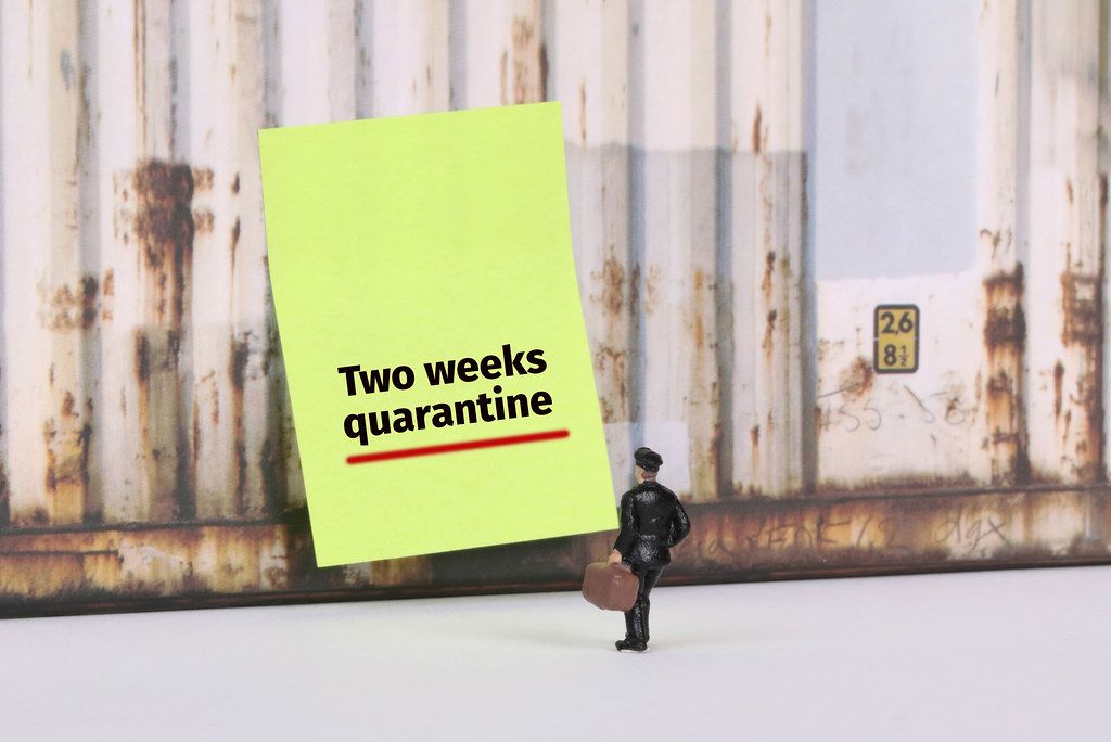 Man with a suitcase standing in front of yellow board with Two weeks quarantine text