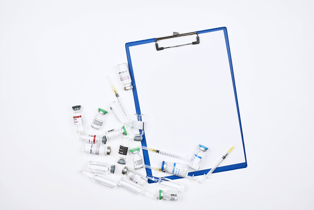 Many different ampoules with Covid-19 vaccine and a clipboard on a white background with space for text